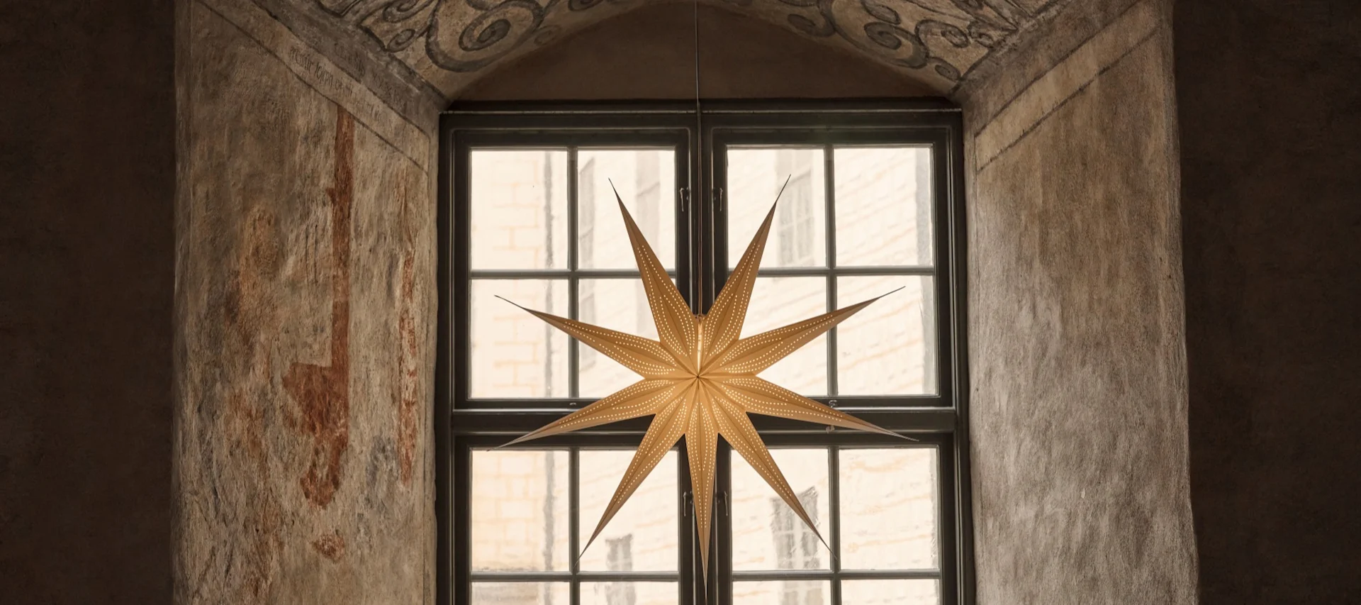 Een verlichte, meervoudige ster hangt in een boograam met sierlijke geschilderde ontwerpen erboven.