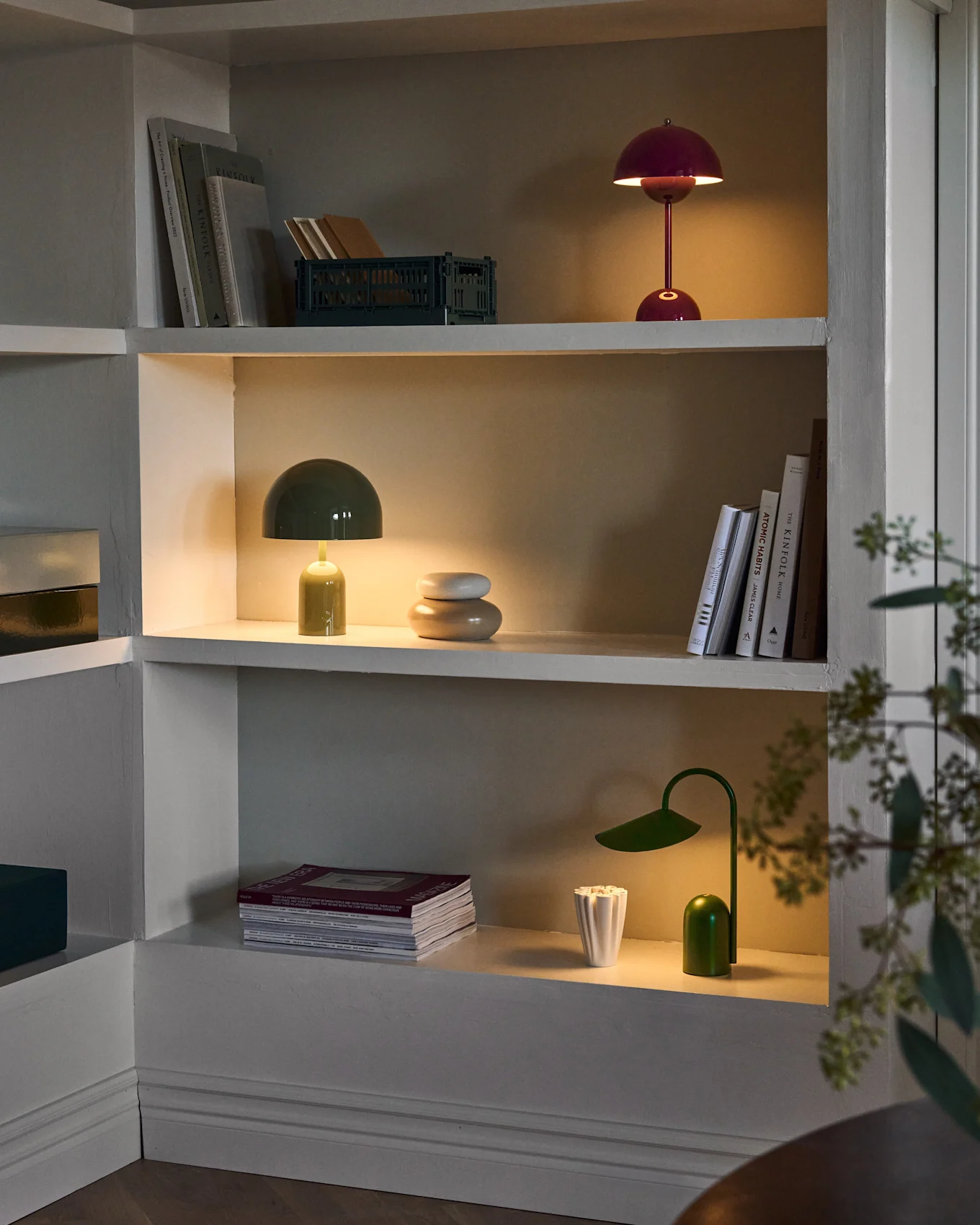 Verlichte planken in ingebouwde kast, met rode en groene paddenstoellampen, groene bureaulamp, boeken en decor.