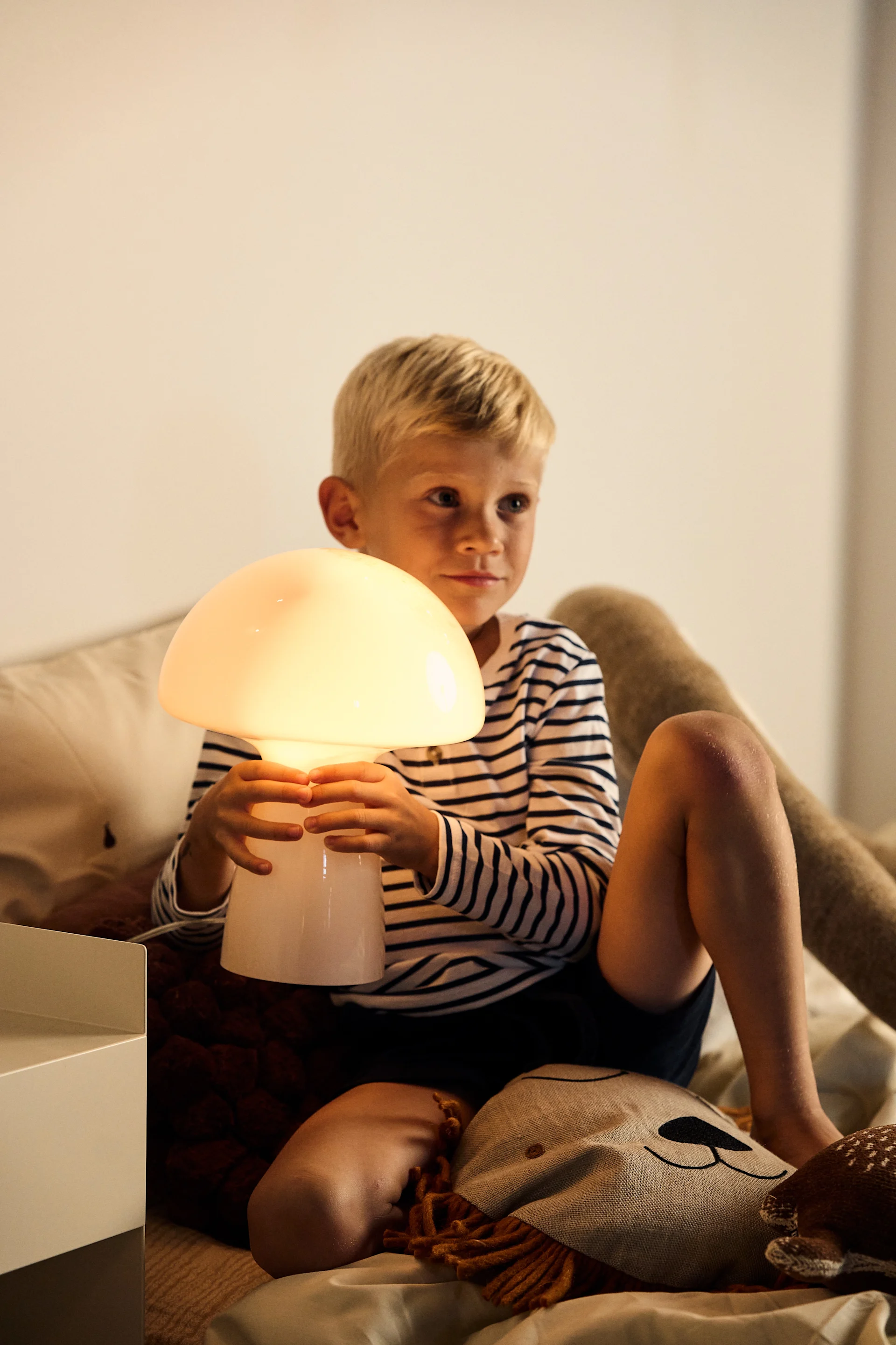Kinderkamers inrichten met verlichting is belangrijk om aan hun behoeften te voldoen, of het nu gaat om licht om te spelen of om te lezen. Hier is de Fungo tafellamp in beige van Globen Lighting, een draagbare lamp in de vorm van een paddenstoel.