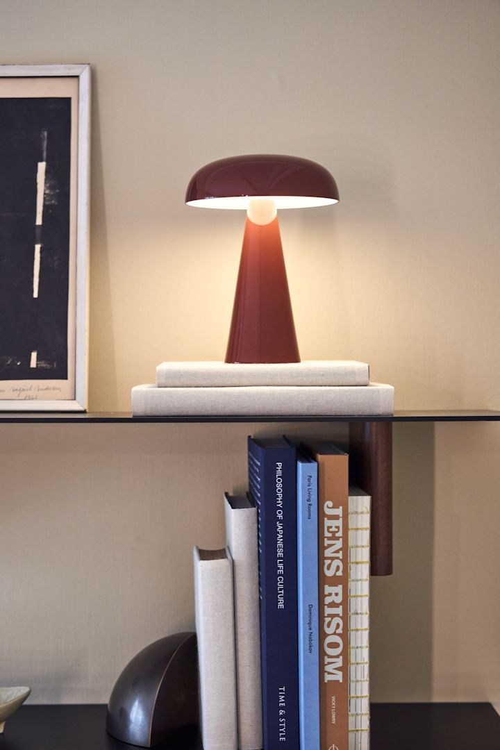 Como draagbare en oplaadbare lamp in rood van &tradition op een stijlvolle boekenplank omringd door boeken. 
