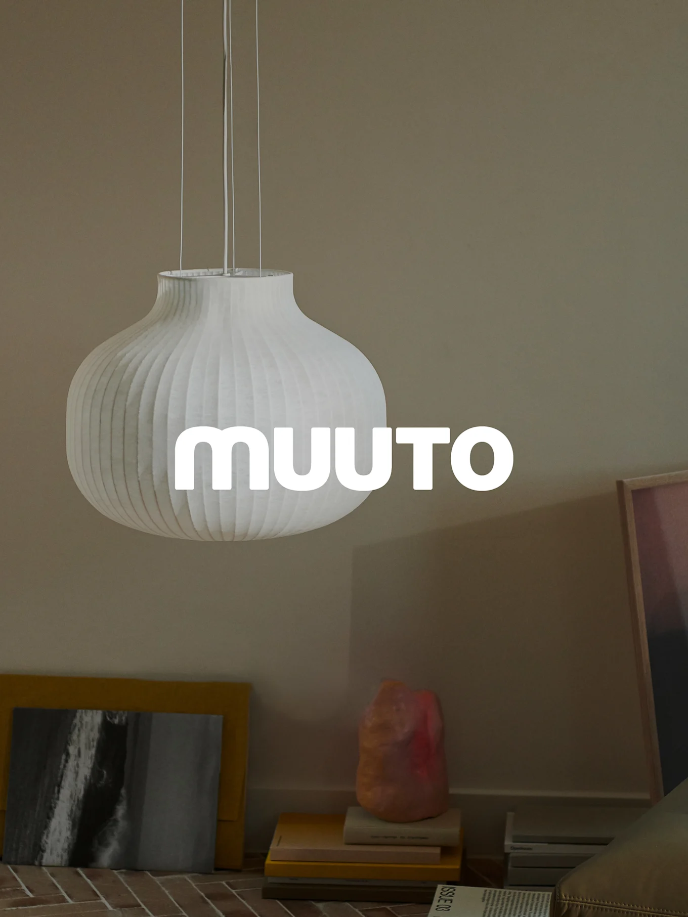 Witte geribbelde pompoenvormige hanglamp met 'MUUUTO'-logo, in een beige kamer.