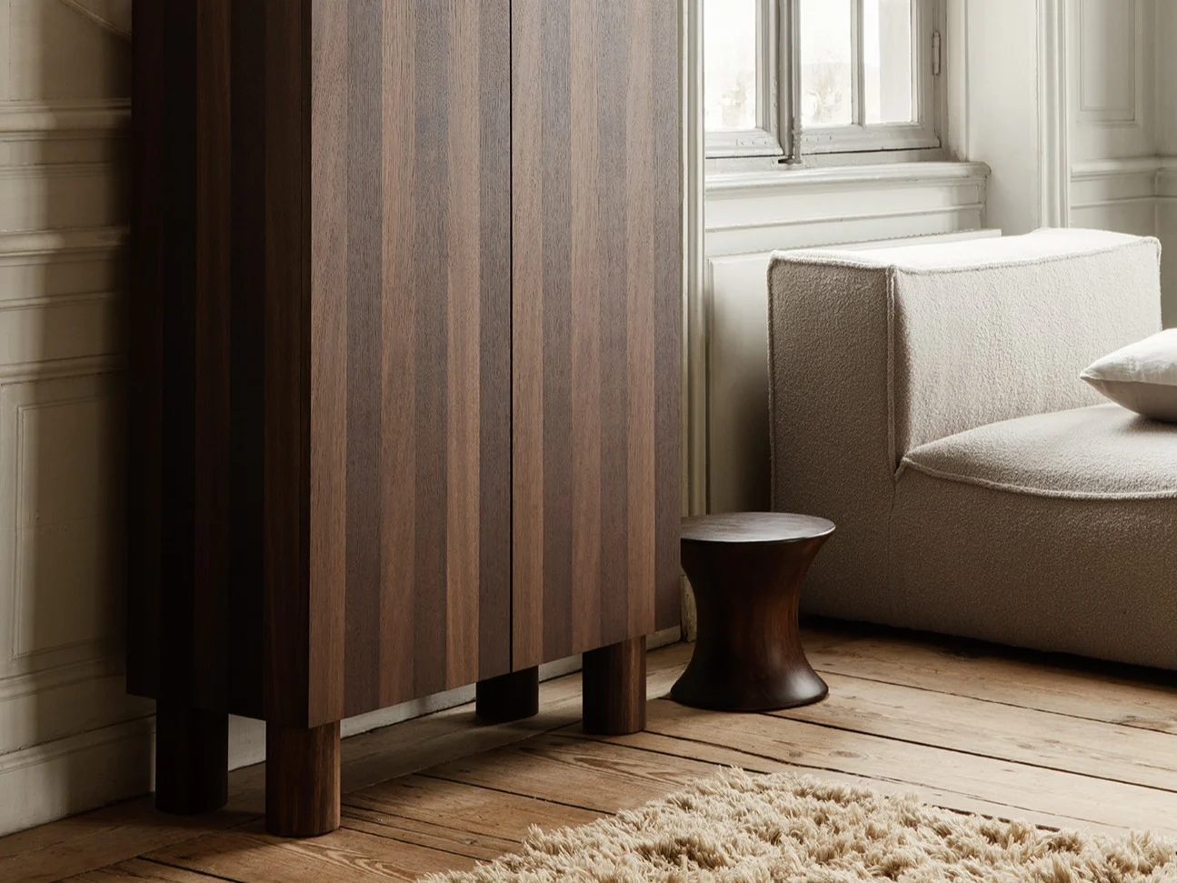 Elegante kamer met donkerhouten gefluteerde kast, sculptuur van knielende vrouw, lichte modulaire bank en groot raam.