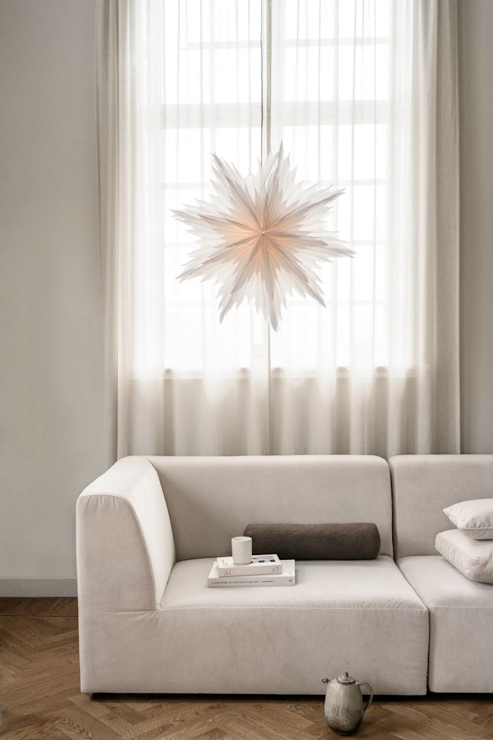 Minimalistische kerstdecoratie zoals de papieren kerstster Oslo van Watt & Veke. Hier te zien hangend in het raam van een neutraal gekleurde woonkamer.