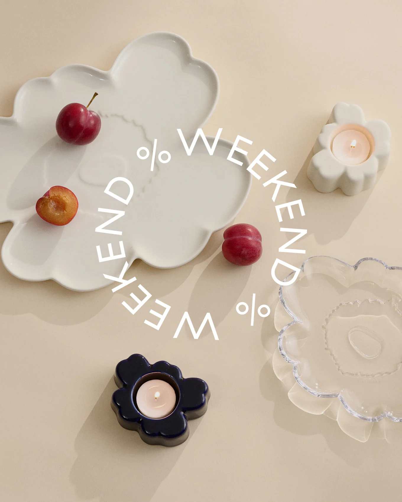 Decoratieve borden en kaarsenhouders in wit, blauw en helder glas met pruimen op een beige achtergrond. Witte tekst 'Weekend %'.