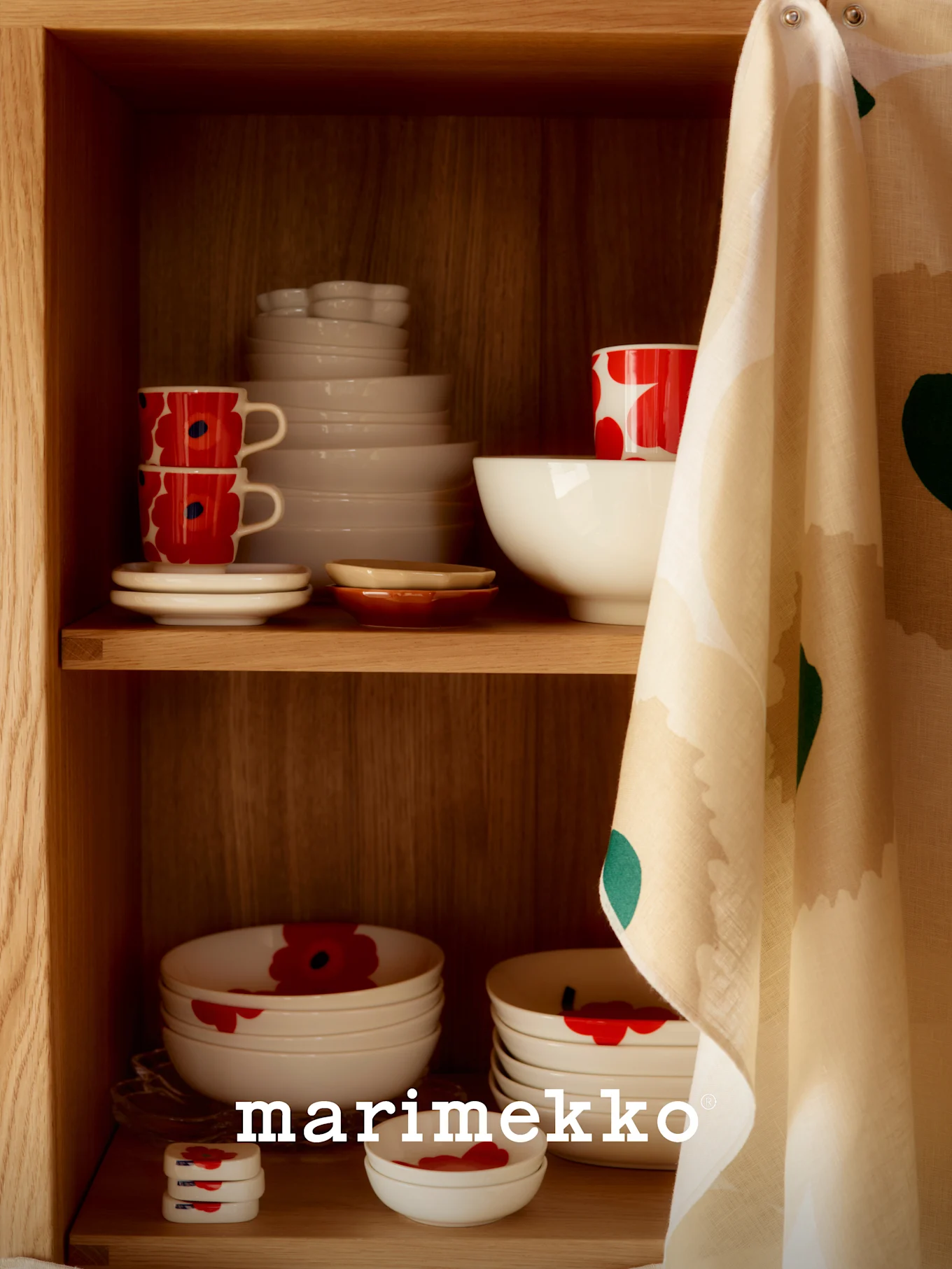 Een houten kastplank met wit keramisch servies, deels met een rood klaproospatroon, en een bedrukte theedoek hangend aan de zijkant.