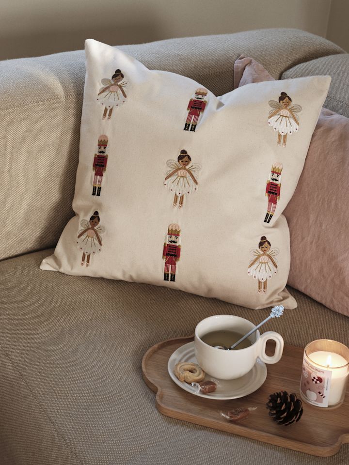 De sprookjesachtig geborduurde kussenhoes van Broste Copenhagen, hier op een bank, is een van de trends in kerstdecoratie 2025.