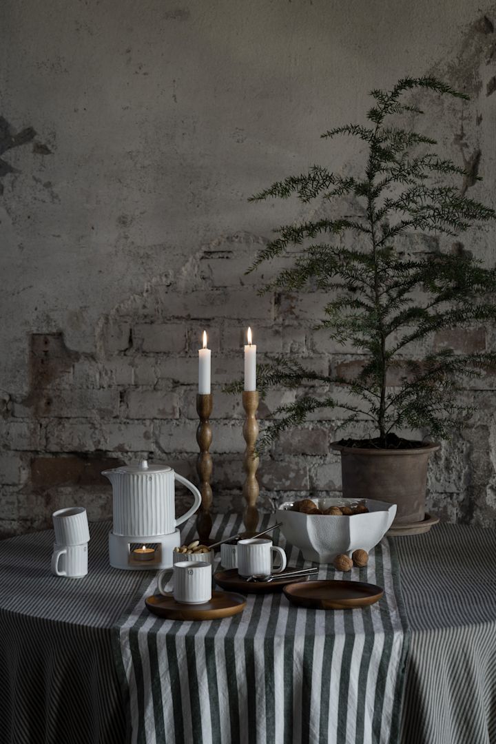 Een gedekte tafel met servies, een kan, kandelaars en Ernsts groen-wit gestreept tafelkleed.
