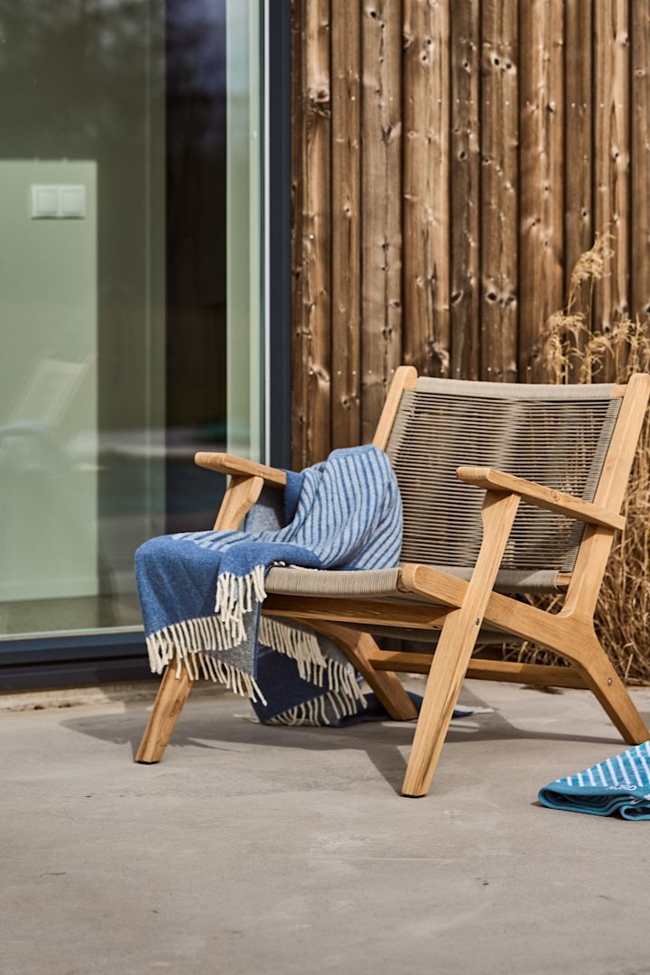 Een Scandinavisch terras met de Sandvik loungestoel uit 1898 en de blauwe Stripes wollen deken van NJRD.