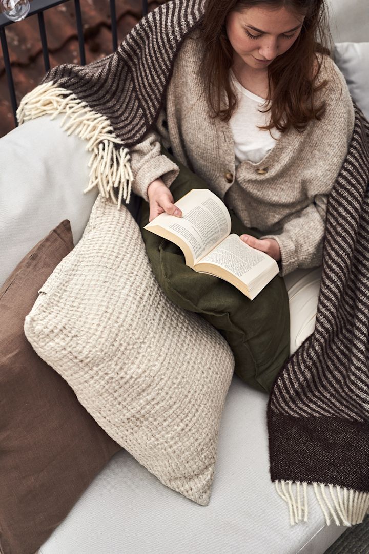 Een vrouw zit op een bank op het balkon een boek te lezen.
