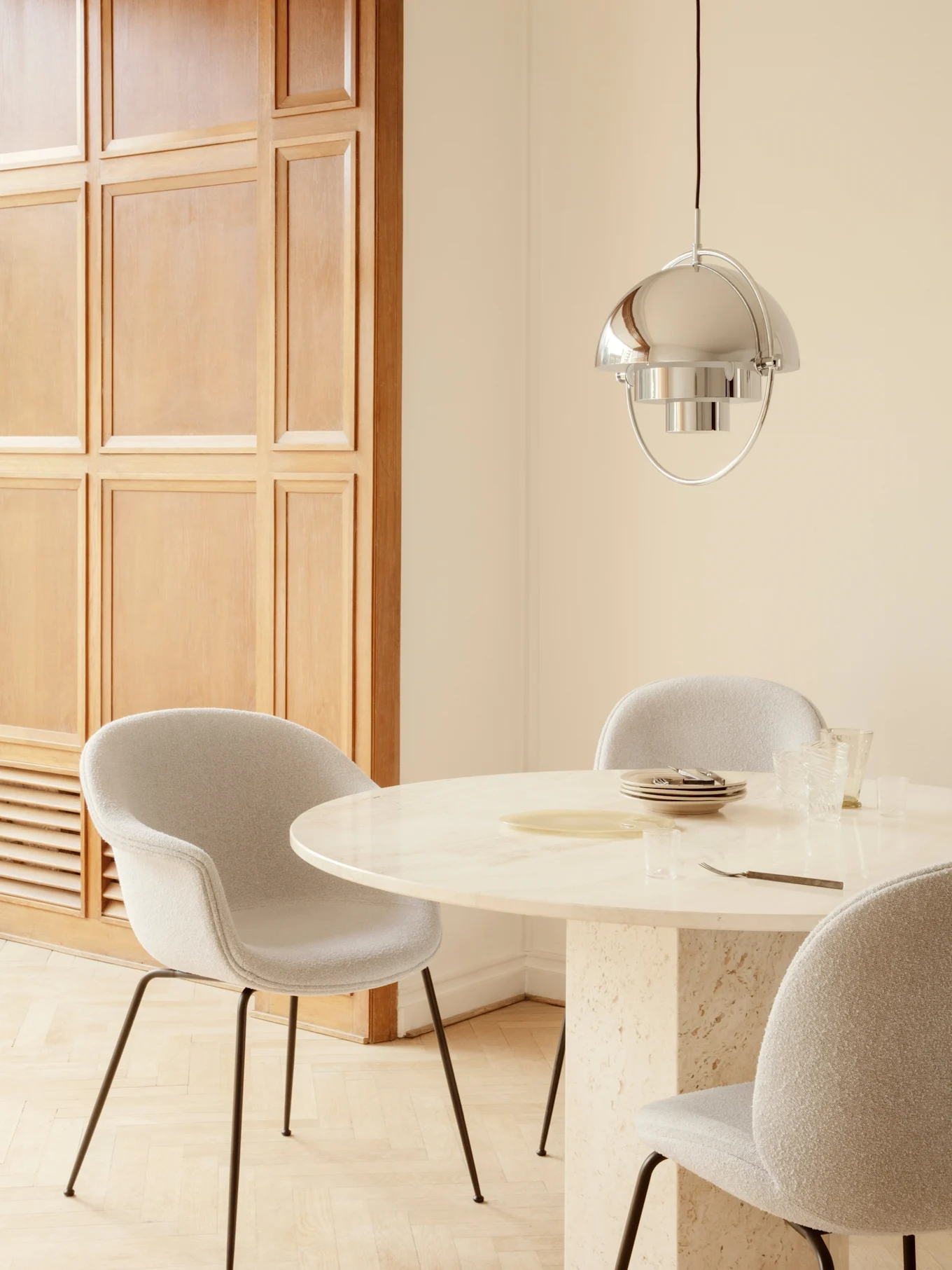 Eetkamer met ronde marmeren tafel, lichtgrijze gestoffeerde stoelen en een gepolijste zilveren hanglamp.