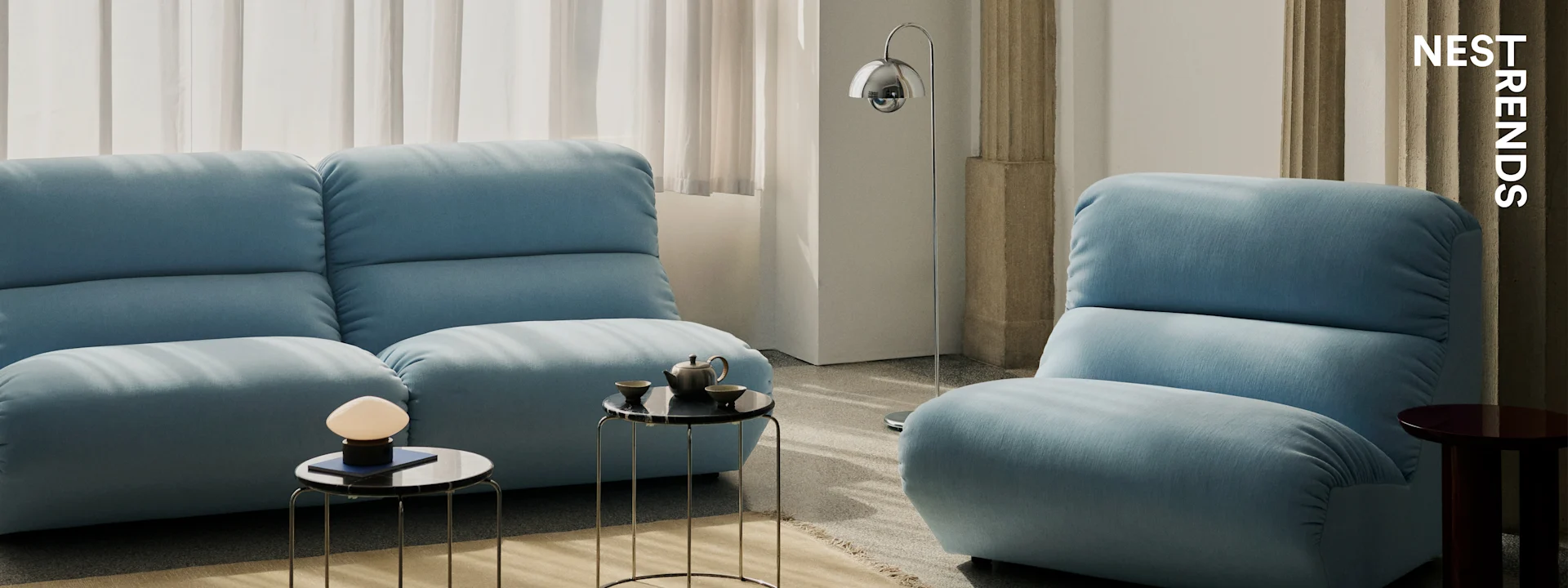 Moderne woonkamer met twee lichtblauwe banken, zwarte marmeren bijzettafels en slanke lampen.