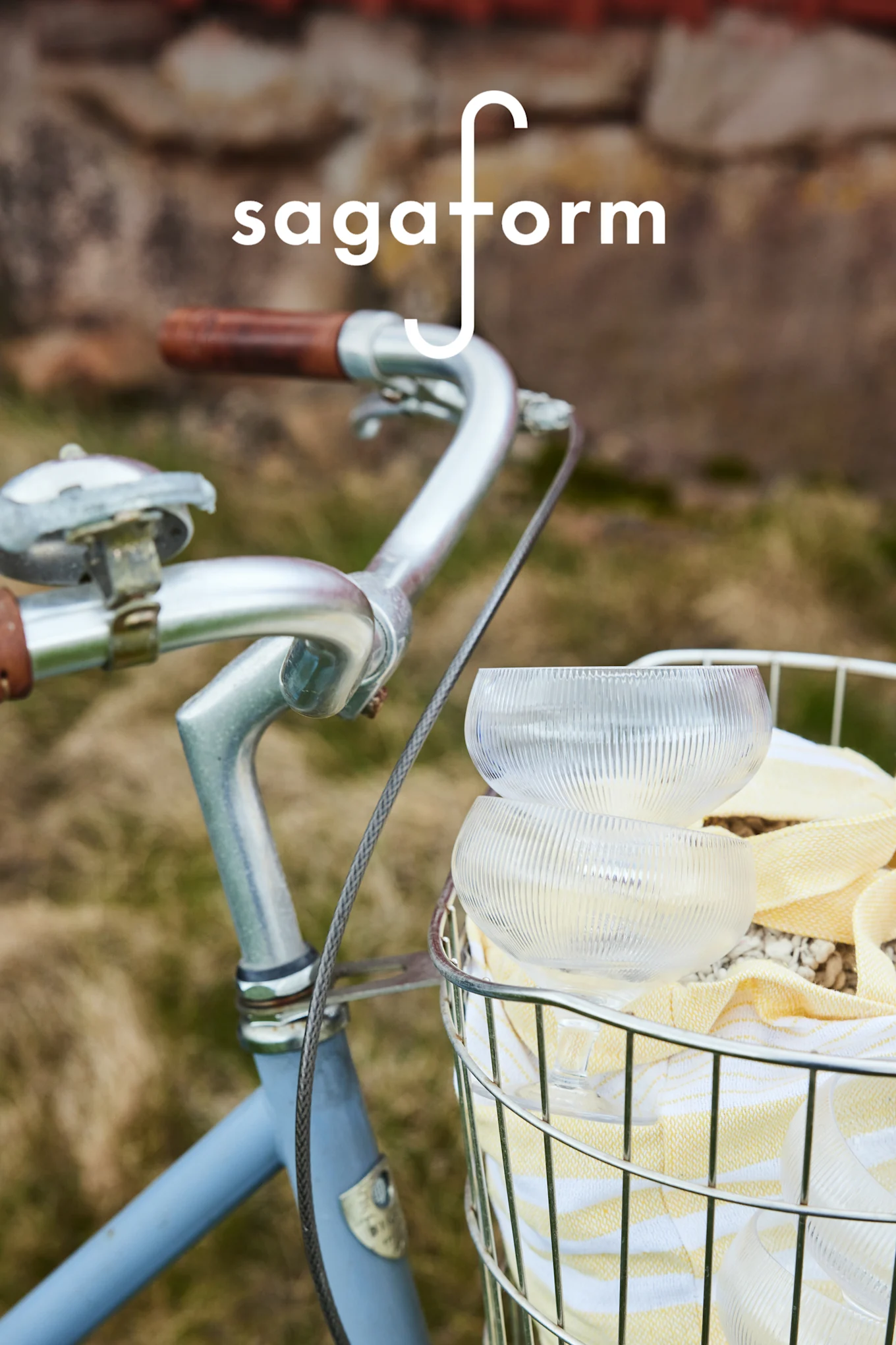 Twee heldere, geribbelde glazen kommen en een geel gestreepte handdoek in een fietsmand. 'sagaform'-logo.