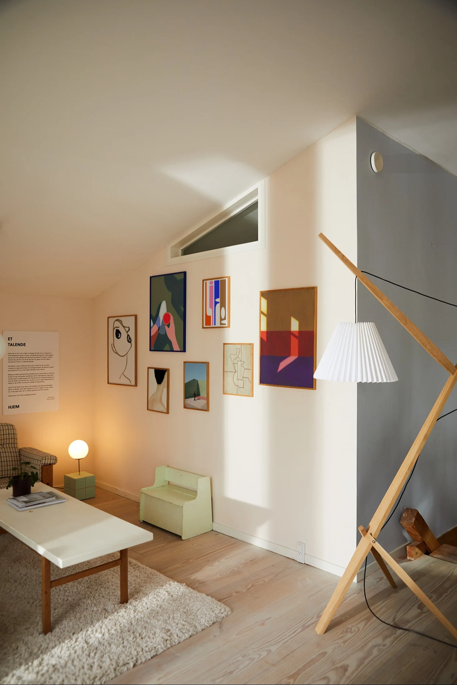 Lichte woonkamer met galerijmuur van abstracte kunst, witte salontafel, geruite fauteuil en houten vloerlamp.