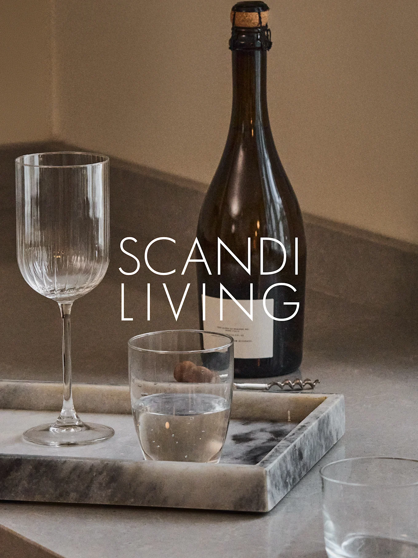 Een donkere fles, een geribbeld wijnglas, een waterglas en een kurkentrekker op een marmeren dienblad met de tekst 'SCANDI LIVING'.