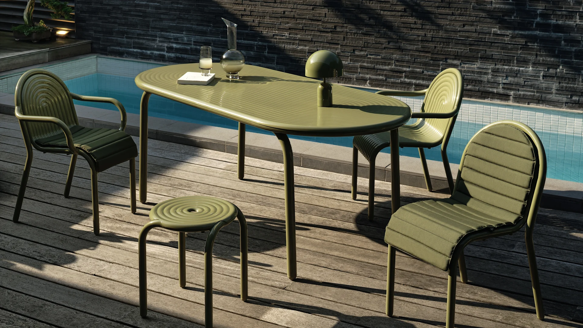 Gedempt groen buitenmeubelset met ovale tafel, drie gestoffeerde stoelen en een kruk op een houten terras bij een zwembad. Een lamp, karaf en glas op de tafel.