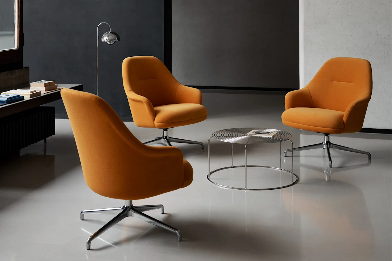 Drie oranje draaibare fauteuils rond een ronde chromen salontafel in een moderne kamer.