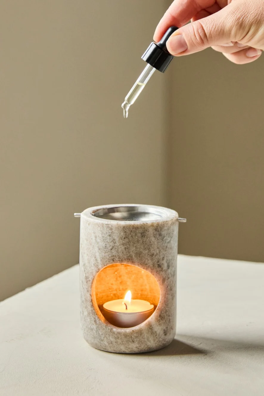Hand druppelt etherische olie in een brandende stenen diffuser.