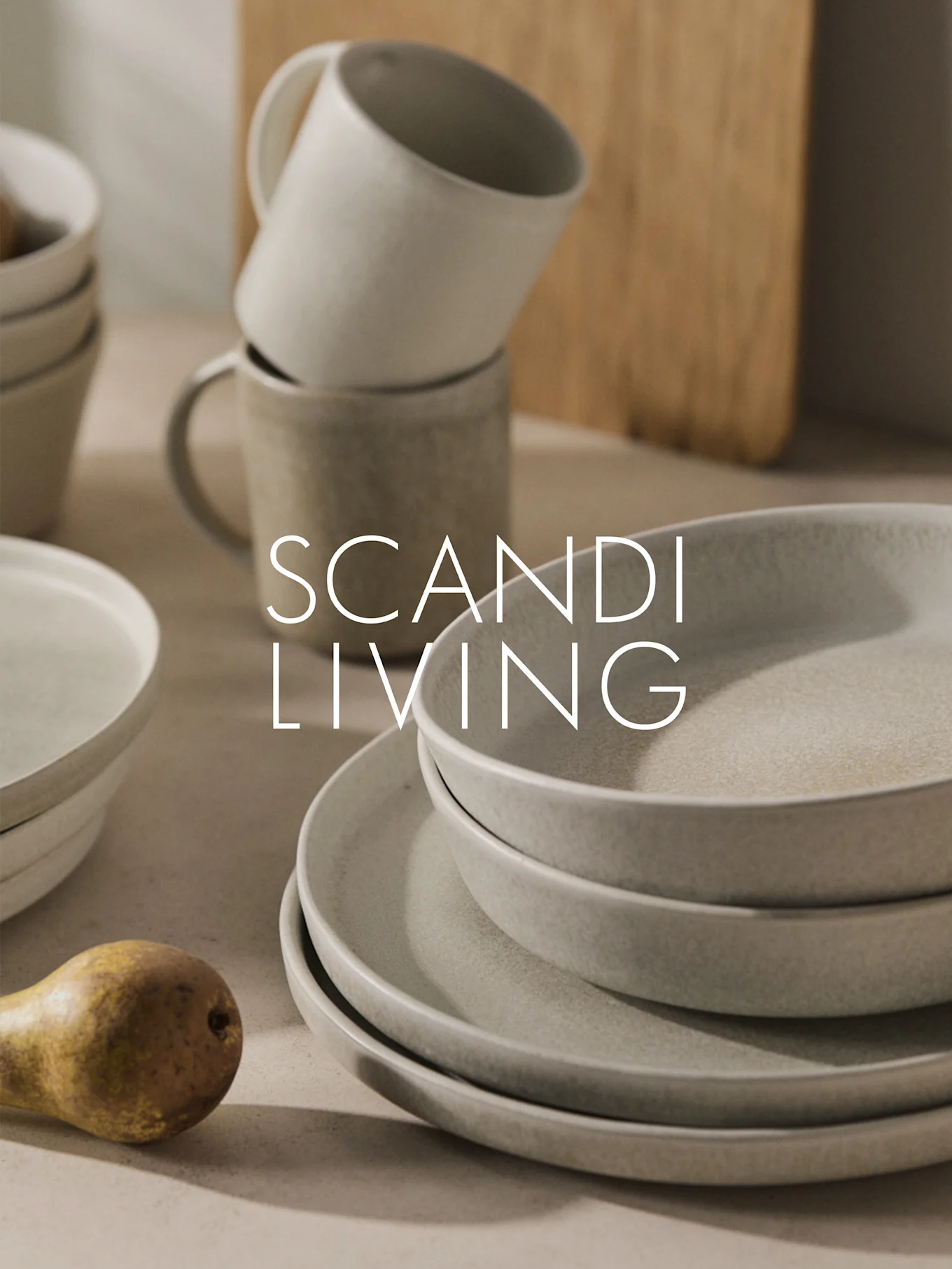 Gestapeld beige keramisch servies, mokken en een peer met "SCANDI LIVING" tekst.
