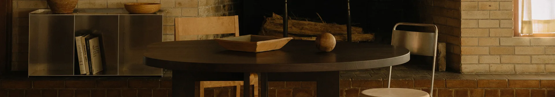 Een gezellige eethoek met een ronde donkere houten tafel, een houten kom, een ovaal object, stoelen en een open haard.