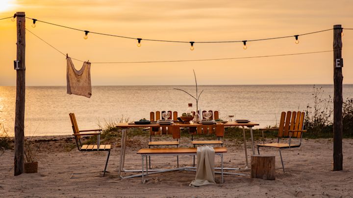 Maak kennis met Grythyttan Stålmöbler, hier A2 stoelen en A1 tafel op het strand bij zonsondergang.