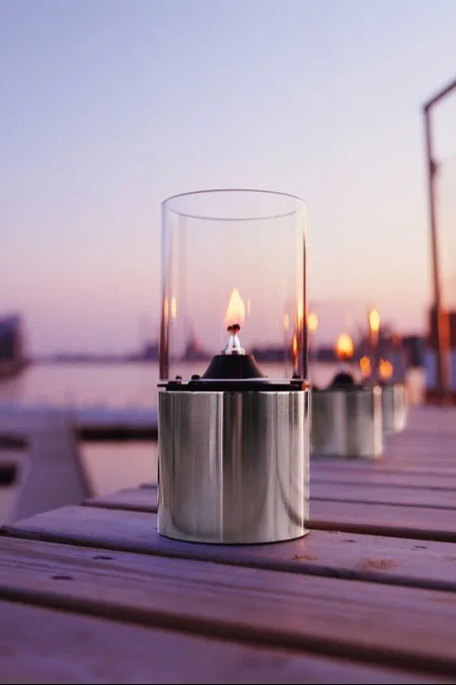 Plaats buitenlantaarns en windlichten op je balkon, terras of in de tuin, bijvoorbeeld de stijlvolle olielamp van Stelton.
