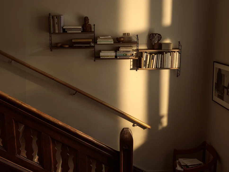 Zonovergoten muur met houten planken vol boeken en decoratie, naast een houten trap en leuning.