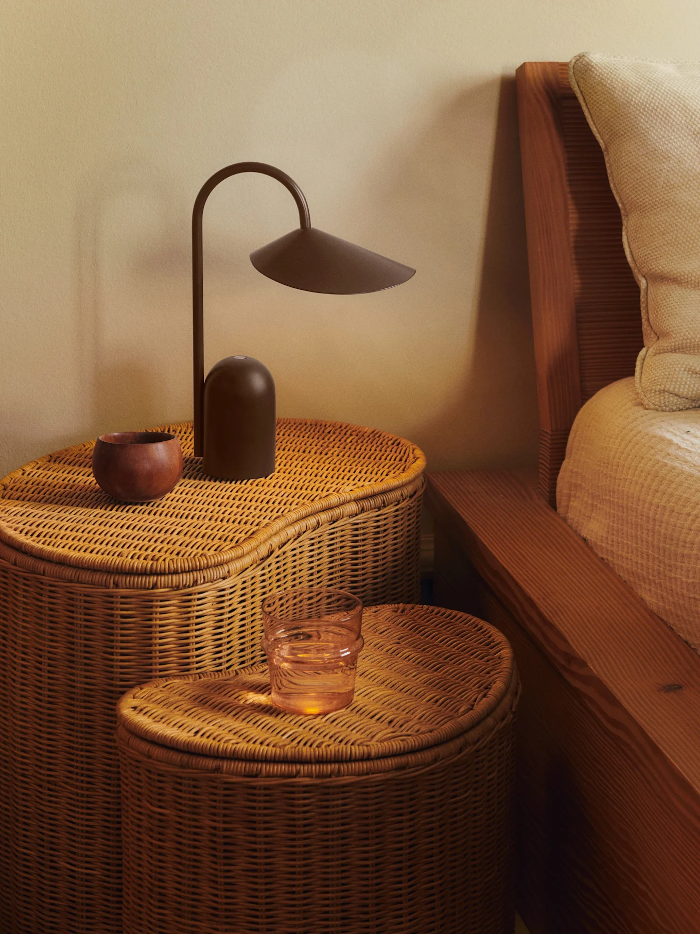Twee gevlochten rotan nachtkastjes met een donkerbruine lamp, een houten kom en een glas water.