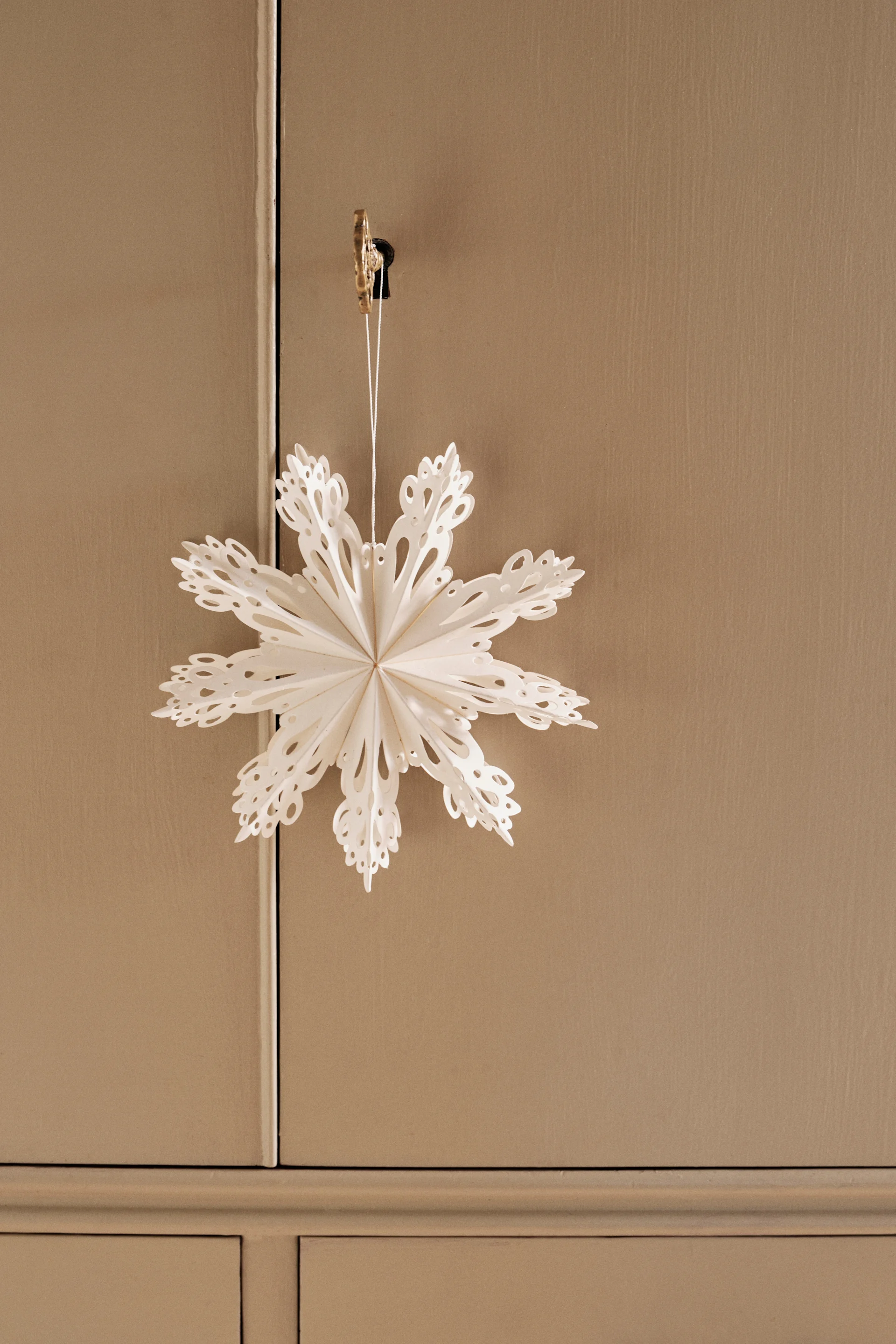 Rustieke woondecoratie met een consoletafel, stoel, vaas met groene takken, een geplooid papieren sterornament en brandende kaarsen op linnen doek.