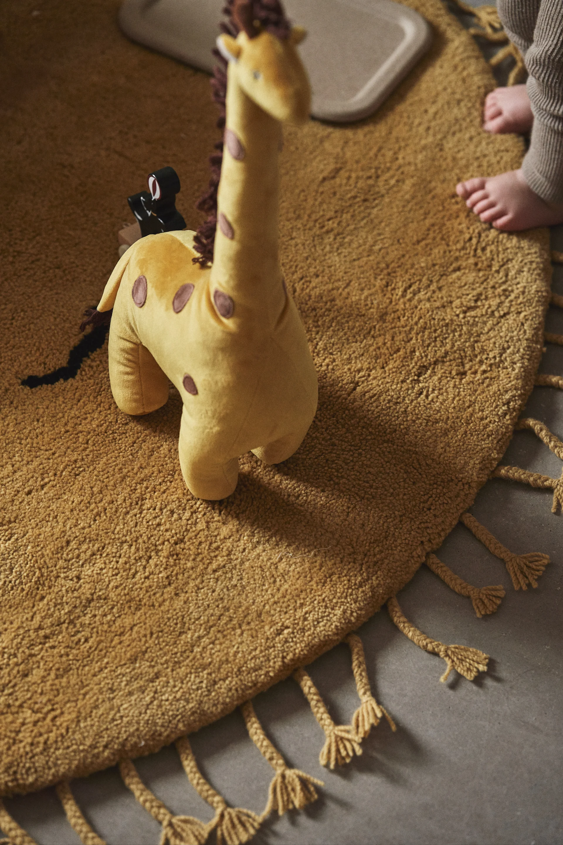 Het is een geweldig idee om kleur in een kinderkamer te brengen met knuffels en andere accessoires. Hier zie je een giraffe van Bloomingville op het zonnekleed van ferm LIVING. 