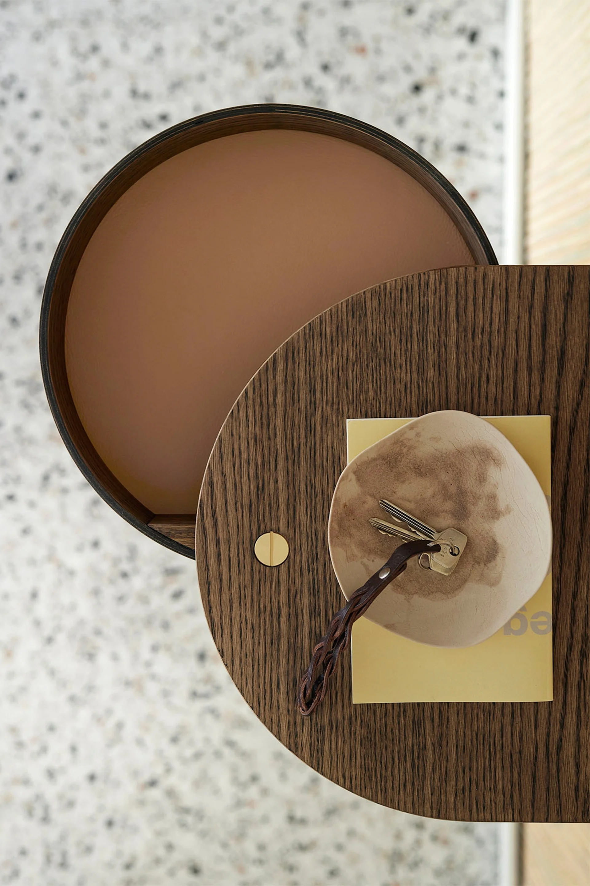Bovenaanzicht van een ronde houten tafel met sleutels op een schaal en een geel boek.