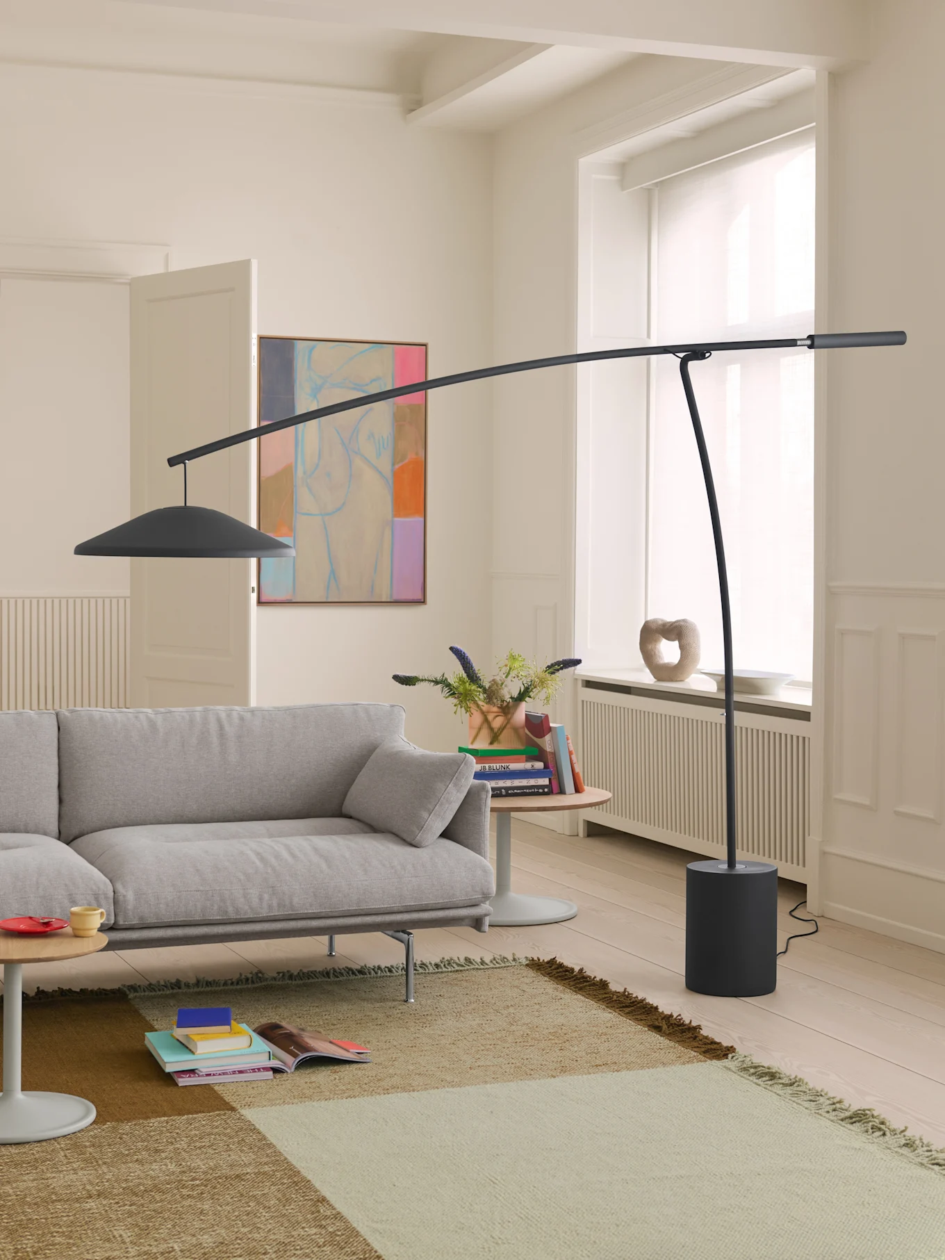Moderne woonkamer met lichtgrijze bank, hoge donkergrijze booglamp en een patroonkleed op lichte houten vloer.