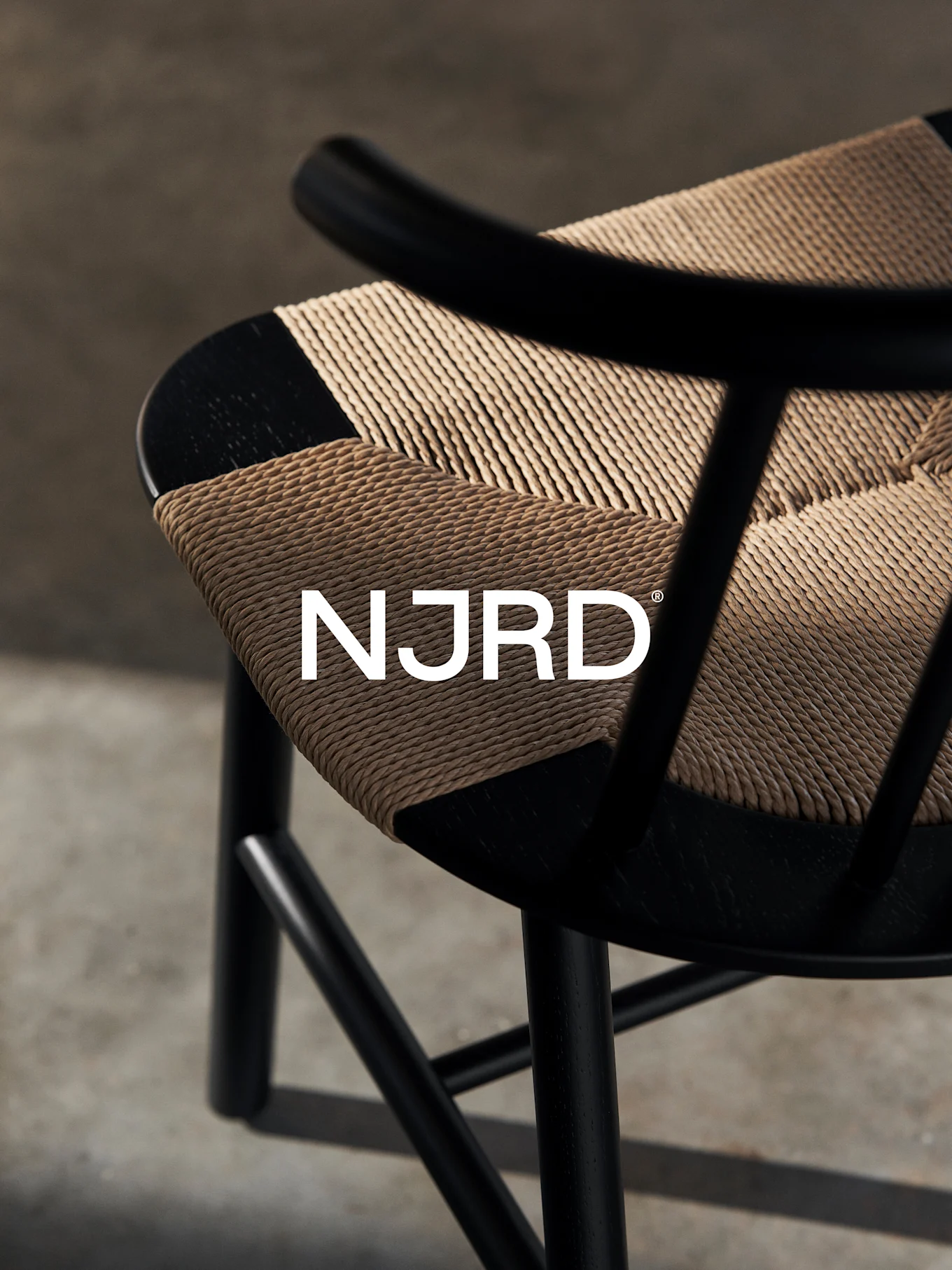 Close-up van een zwarte stoel met een geweven lichtbruine zitting, met het witte 'NJRD'-logo.