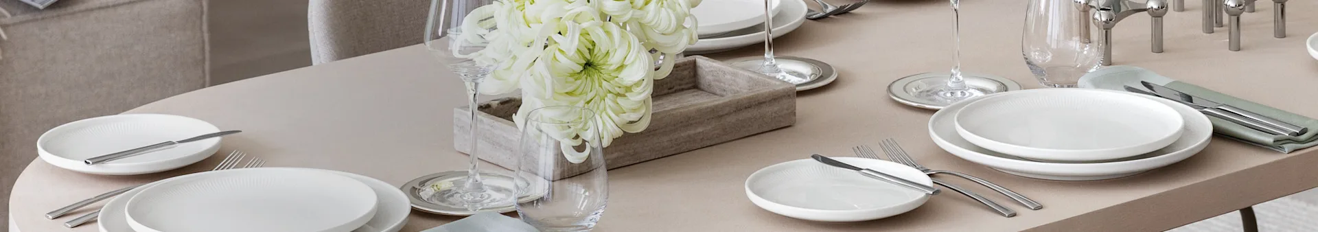 Een elegant gedekte eettafel met witte borden, zilver bestek, wijn- en waterglazen, en een centerpiece van grote witte bloemen in een houten kist.