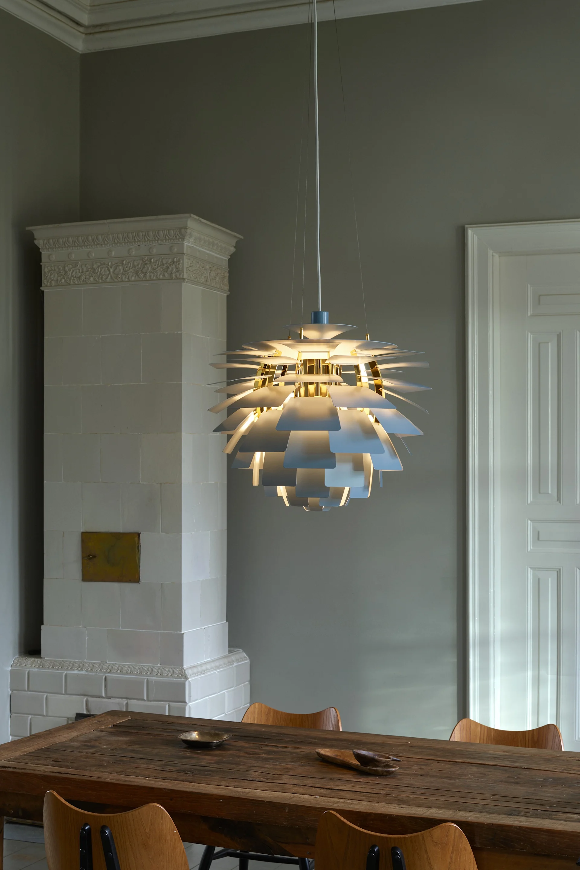 Een stralende, meerlagige hanglamp met witte en gouden accenten verlicht een rustieke houten eettafel.