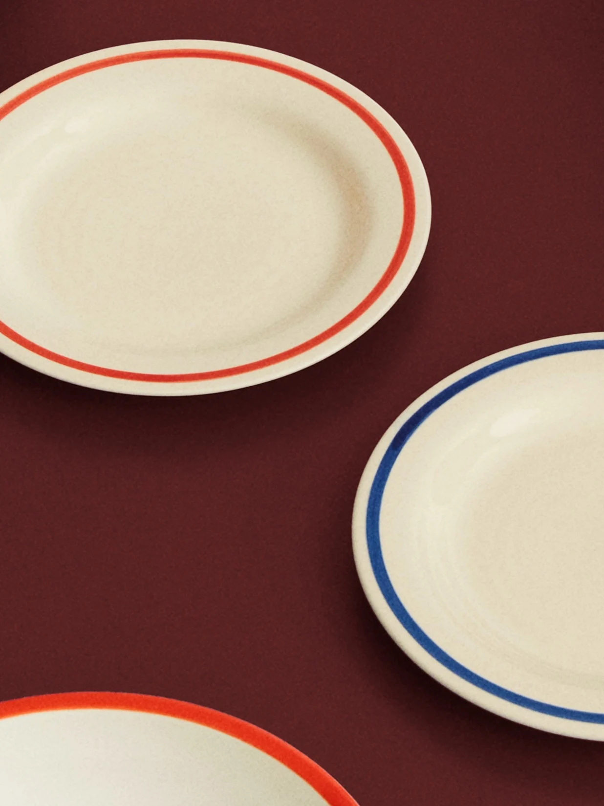 Drie crèmekleurige ovale borden met rode en blauwe randen op een donkerrode ondergrond.