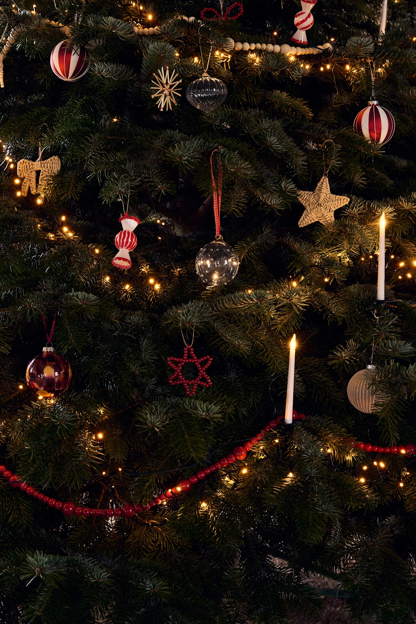 Een rijk versierde kerstboom met diverse ornamenten, warme lichtslingers en gloeiende kaarsjes.