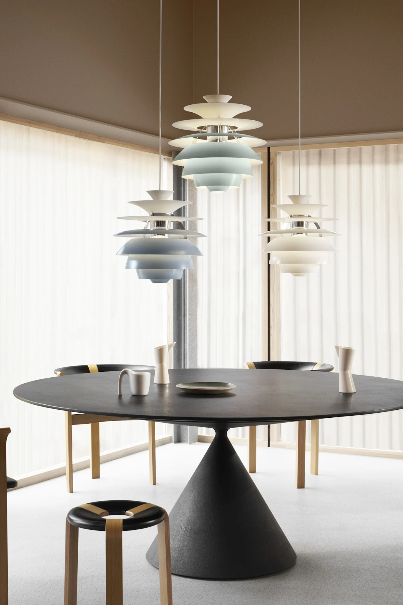 Moderne eetkamer met ronde zwarte tafel, stoelen en drie gelaagde hanglampen, twee blauw en één wit.