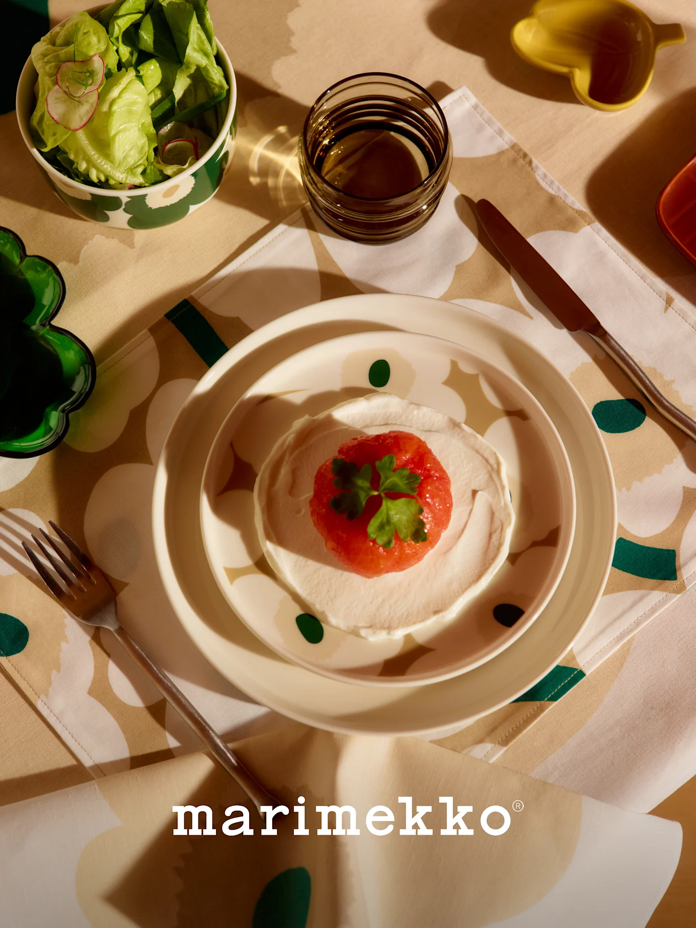 Marimekko tafelschikking met gedessineerde slakom, rood fruit- en roomgerecht, glas en bestek op een bloemen tafelkleed.