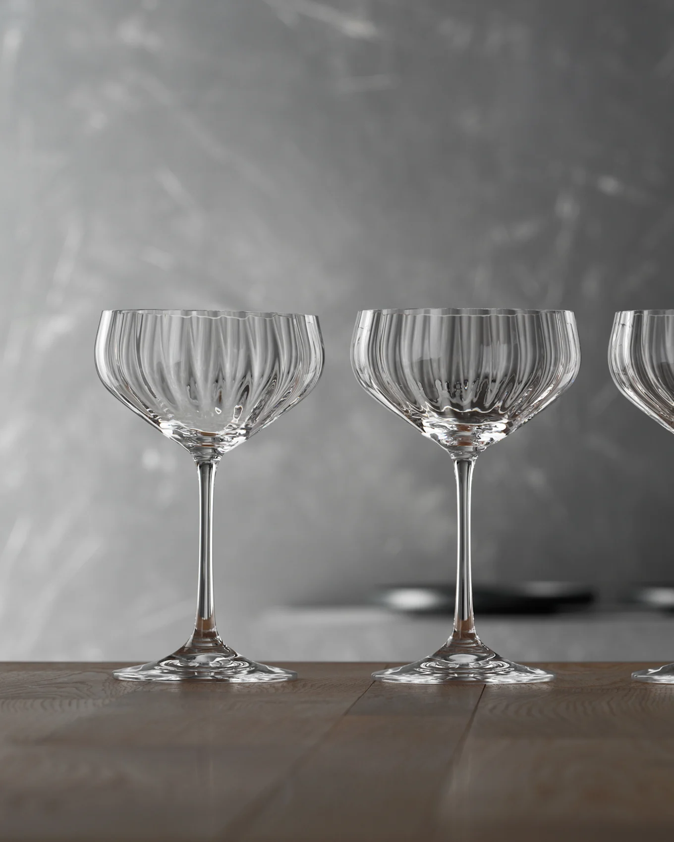 Drie lege, heldere geribbelde champagneglazen op een houten tafel tegen een grijze achtergrond.