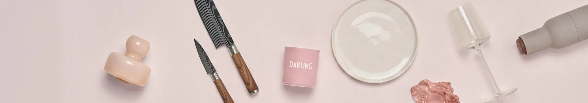 Decoratie op roze: roze vaas, gedessineerde messen, 'DARLING' kaarsenhouder, beige bord, wijnglas, grijze fles.