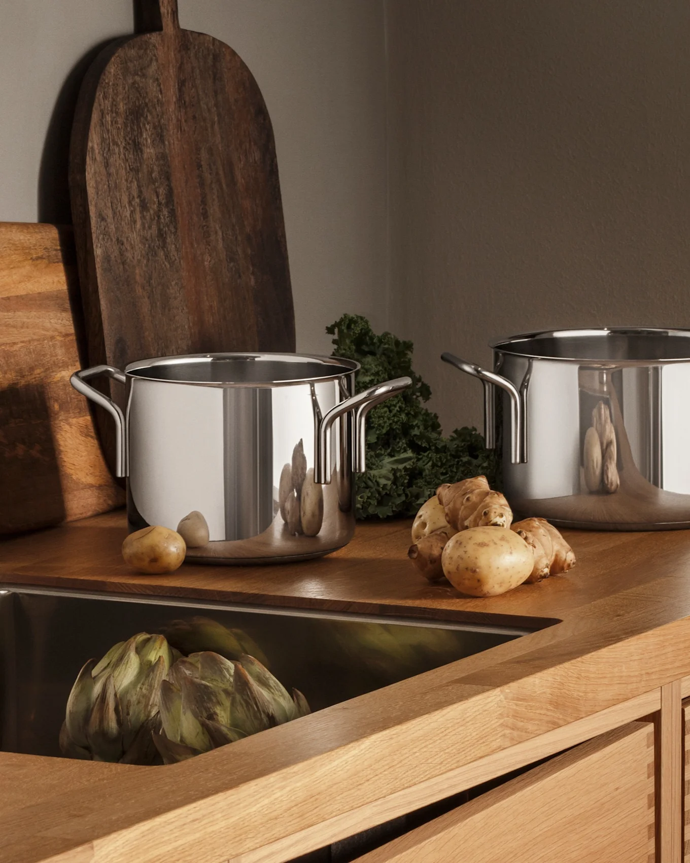 Moderne keuken met houten aanrecht, RVS spoelbak, kraan, drie pannen en verse producten zoals aardappelen en artisjokken.