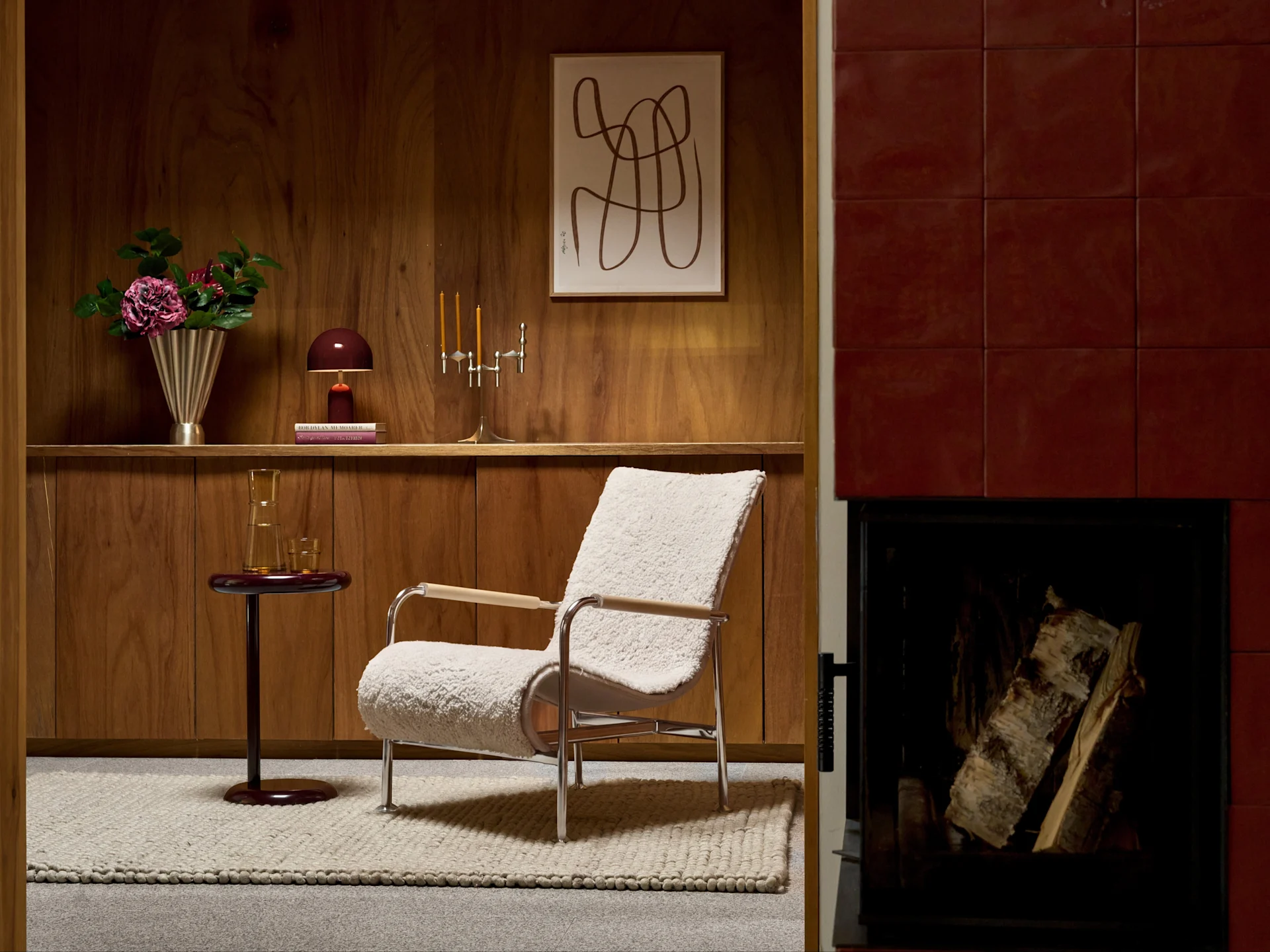 Crèmekleurige bouclé fauteuil met chroom frame in houten kamer, naast een rode tegelhaard met hout.