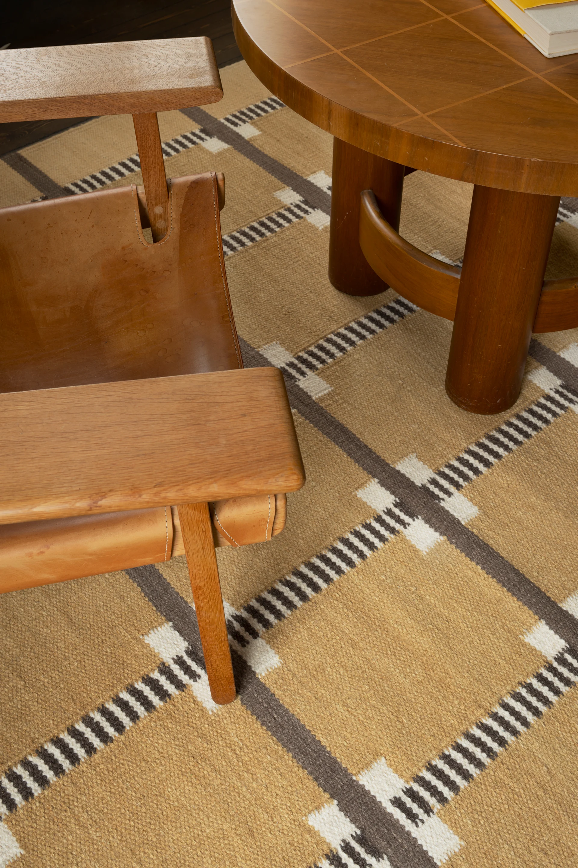 Houten fauteuil met leren zitting naast een ronde salontafel op een geometrisch patroon tapijt.