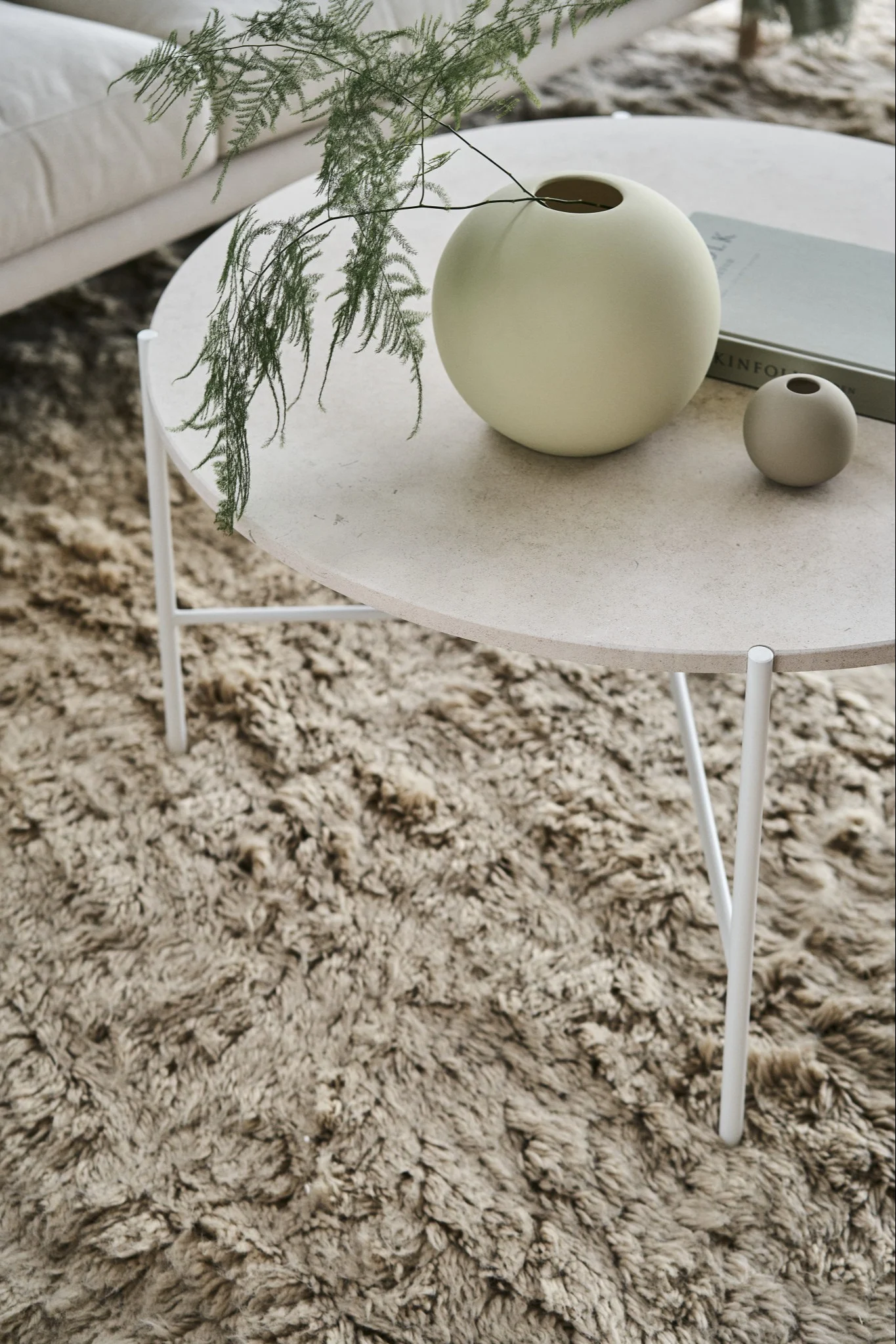De iconische Ball vaas in Shell en Sand van Cooee Design op een bijzettafel in een woonkamer in Scandinavische stijl.