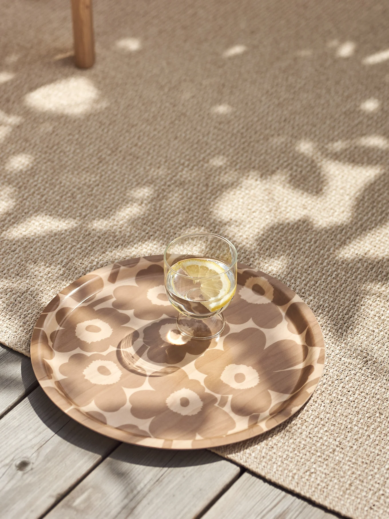 Glas citroenwater op een beige dienblad met bloemenpatroon op een getextureerd vloerkleed met gevlekt zonlicht.
