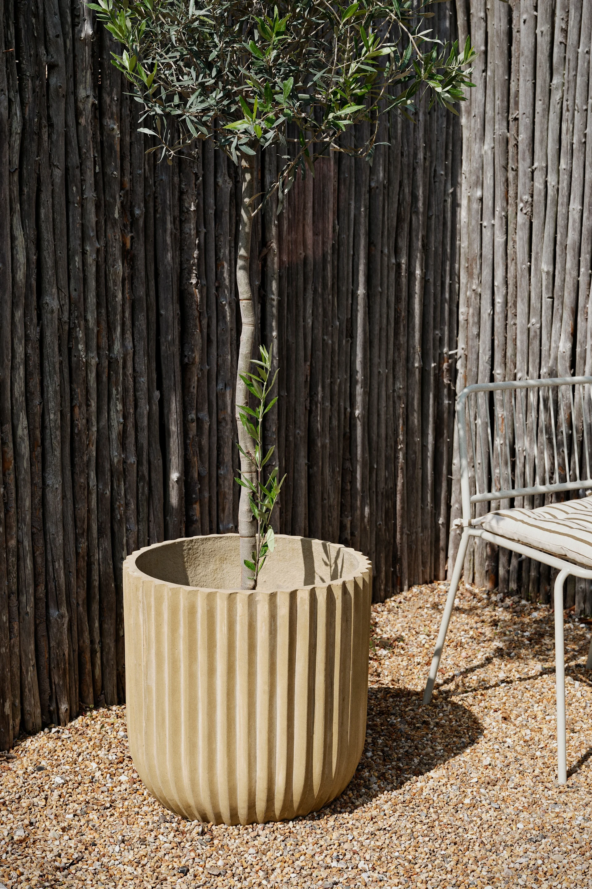 De rustieke fiber buitenpot van Broste Copenhagen staat in een tuin.