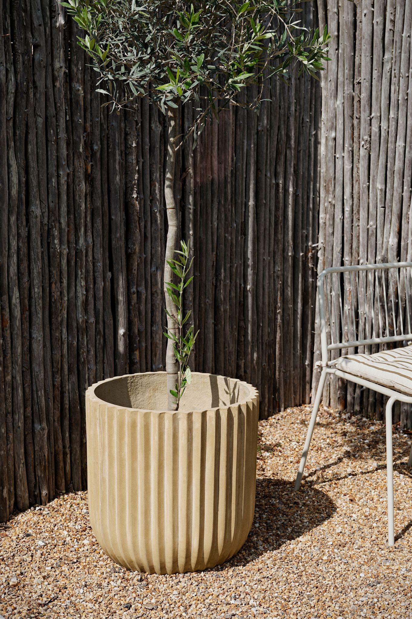 De rustieke fiber buitenpot van Broste Copenhagen staat in een tuin.