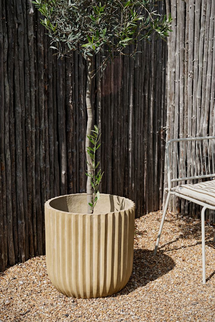 De rustieke fiber buitenpot van Broste Copenhagen staat in een tuin.