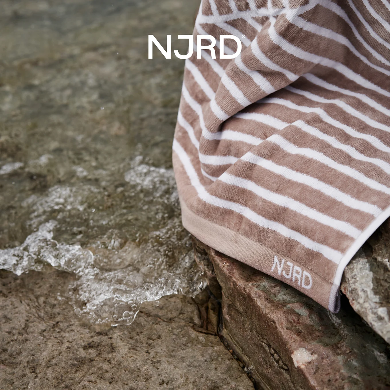 NJRD beige en wit gestreept handdoek op rotsen bij kabbelend water.