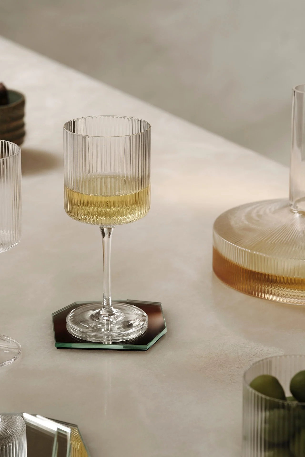 Een geribbeld wijnglas met witte wijn op een zeshoekige spiegelonderzetter.